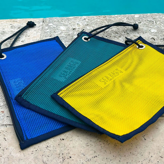 Three Goldenrod Mesh Tote Organizer Pouches by Sea Bags in blue, green, and yellow rest on a stone surface beside a swimming pool—perfect as travel organizers or tote inserts. Made from durable marine-grade mesh, these pouches keep your essentials organized and within easy reach poolside. by Sea Bags