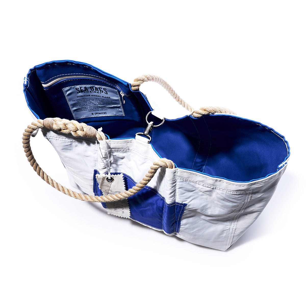 The Sierra Signal Flag Large Tote by Sea Bags is a white and blue tote bag featuring rope handles and a blue interior, made from recycled sail cloth and shown open to reveal the sewn label inside. by Sea Bags