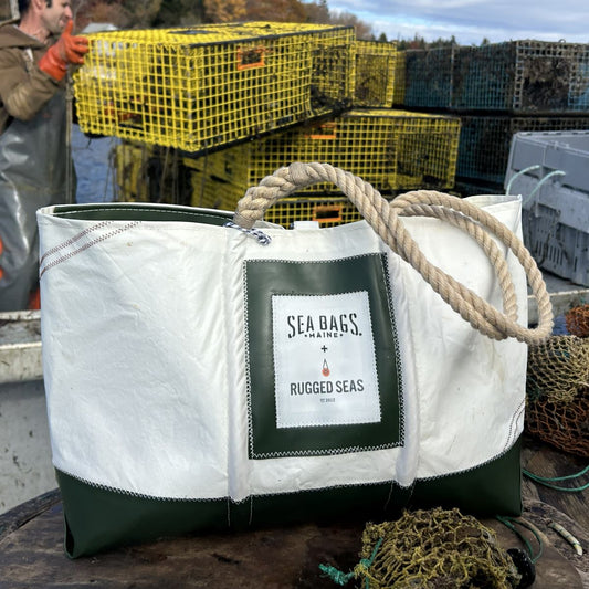 A Trapline Large Tote - Dark Green from Sea Bags, crafted from recycled sail cloth and featuring classic rope handles, rests on a boat beside stacked lobster traps and fishing gear, evoking the rugged spirit of a Maine lobster fisherman. by Sea Bags