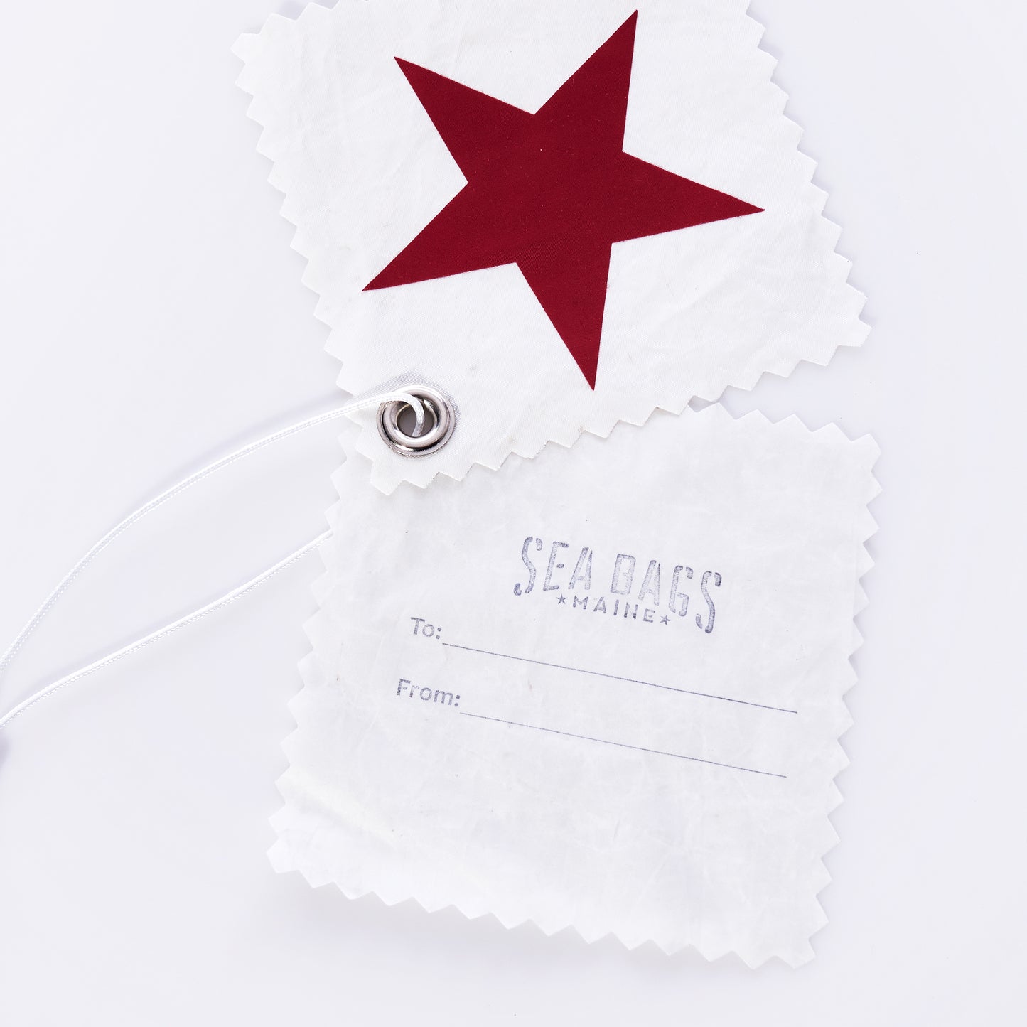 Add a touch of sustainability to your gifts with the Star Sail Cloth Gift Tags from Sea Bags. This set includes two white gift tags crafted from recycled sail cloth—one featuring a red star, and the other stamped with SEA BAGS MAINE and To/From lines. Each eco-friendly tag is finished with zigzag edges, a metal grommet, and a white loop for easy attachment. by Sea Bags