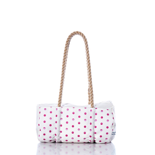 The Flip Side Summer Dots Baguette Bag by Sea Bags features a white tote design adorned with pink polka dots, a cushioned body, and two brown rope handles. Displayed on a reflective surface against a white background, this charming summer handbag blends playful style with everyday practicality. by Sea Bags