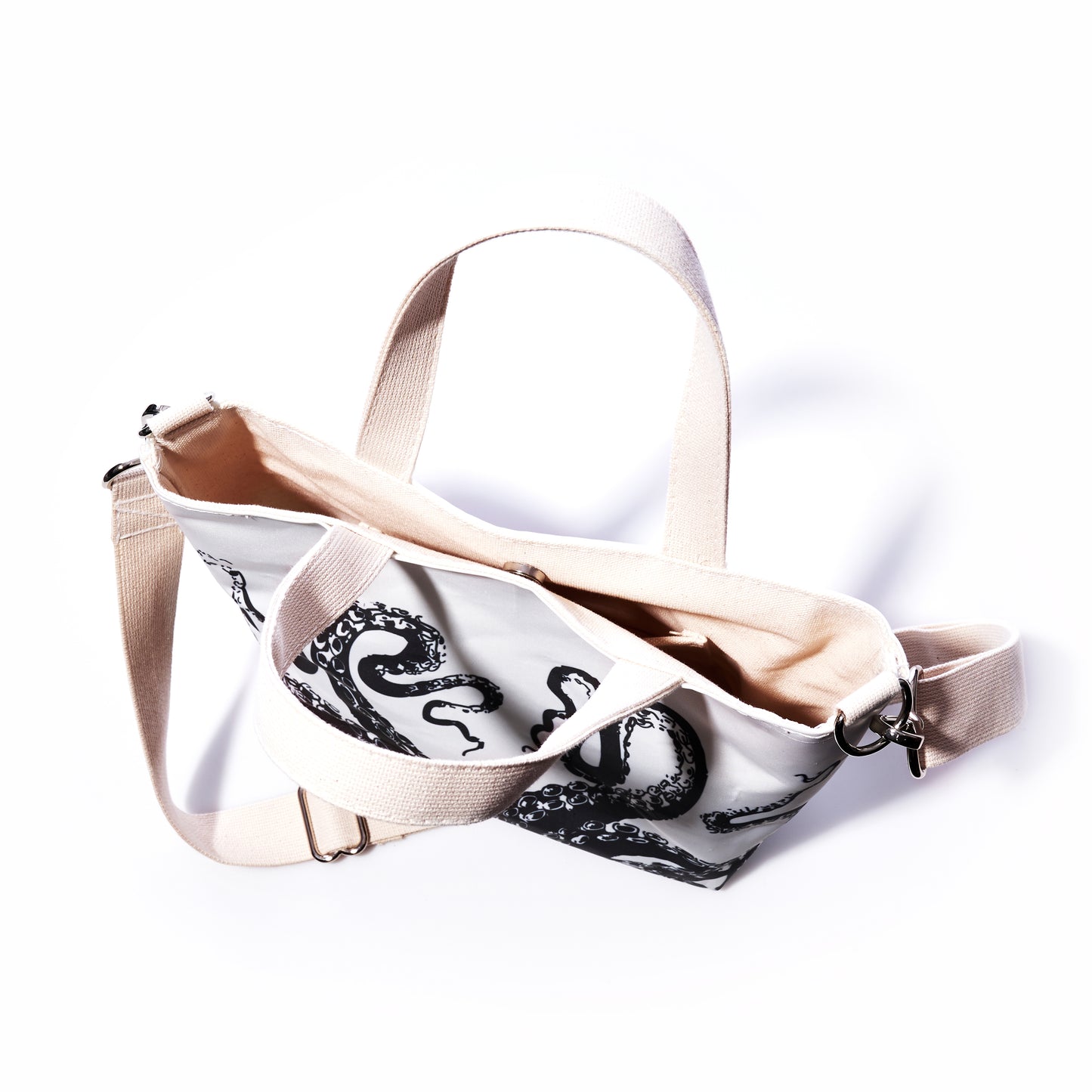 The Sea Bags Octopus Crossbody Tote features a white canvas body with beige straps and a bold black octopus design, pictured from above on a white background. This stylish shoulder bag is both practical and eye-catching—ideal for everyday use. by Sea Bags