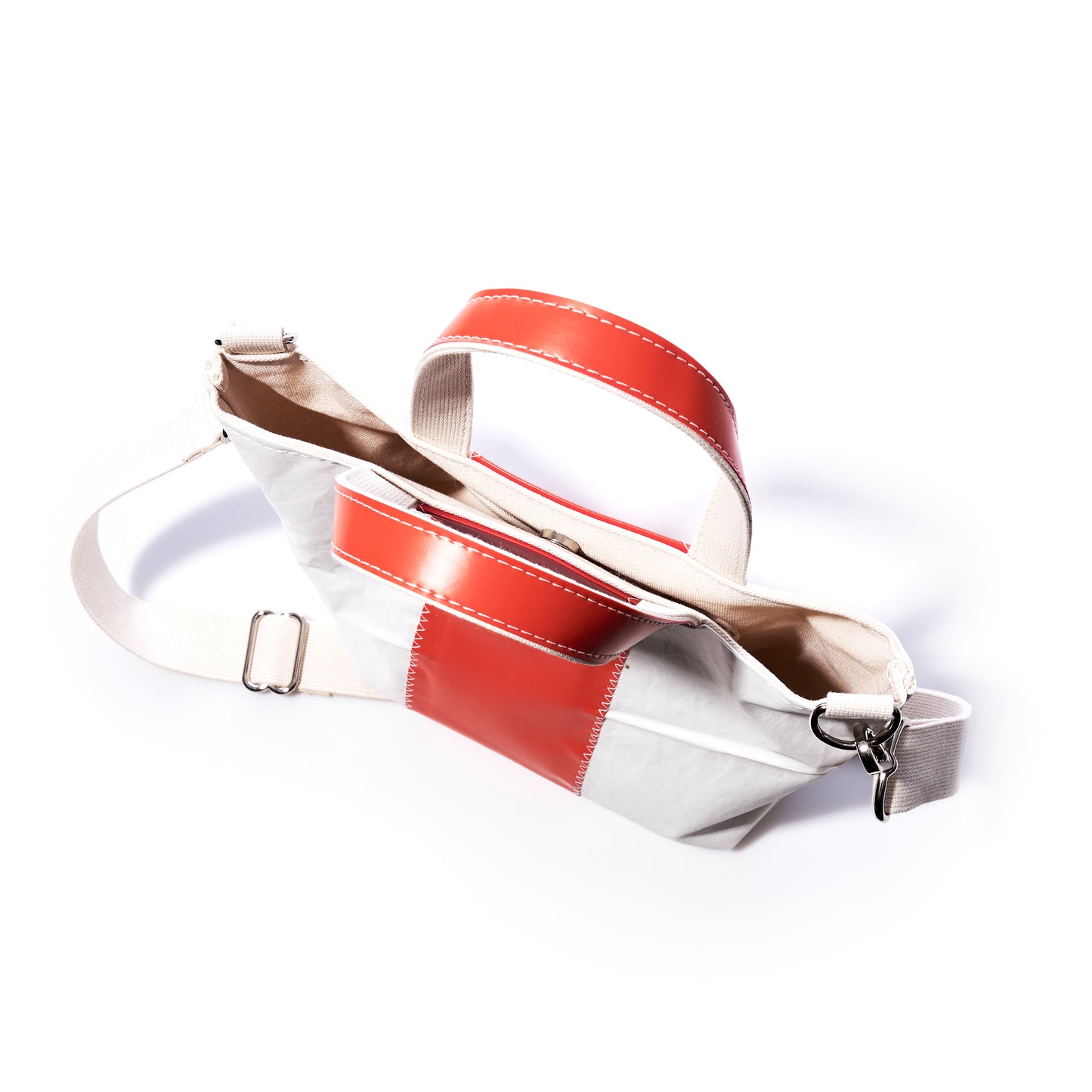 The Sea Bags Trapline Crossbody Tote is a white and red tote bag featuring beige straps, a zippered main compartment, and a metal clasp, shown against a white background. by Sea Bags