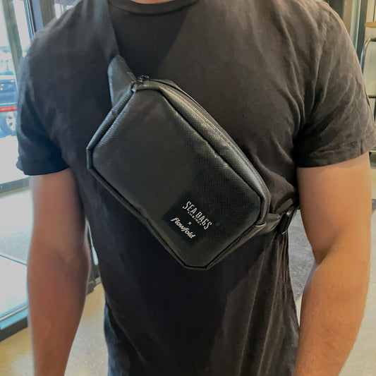 A person wearing a black T-shirt and the Sea Bags Black Dragon Belt Bag for Food52, standing indoors near glass doors. This water-resistant accessory from Sea Bags makes a unique gift for any occasion. by Sea Bags