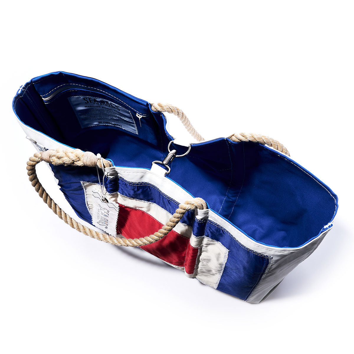 The Sea Bags Whisky Signal Flag Large Tote is a handcrafted bag made from vintage sail cloth, featuring blue, white, and red panels with rope handles. Shown open to reveal the blue interior and inner label. by Sea Bags
