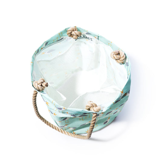 The Sea Bags Wharf Gulls Beachcomber Bucket is a cylindrical fabric bag crafted from recycled sail cloth, featuring a light blue patterned exterior, tan rope handles, and a white interior. Shown from above on a white background, it makes a stylish beach bag option. by Sea Bags