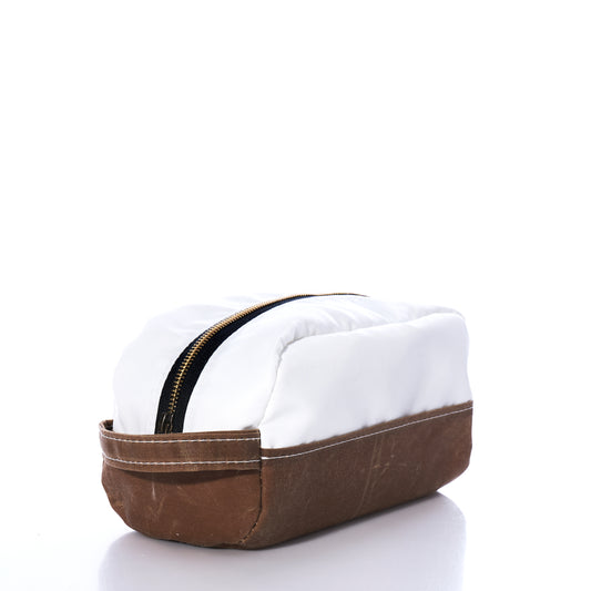 The Tan Chebeague Toiletry Bag by Sea Bags features a rectangular silhouette with a white top and brown waxed canvas base, accented by a visible zipper closure. Set against a white background, its durable design is inspired by seaworthy travel bags—offering both function and style. by Sea Bags