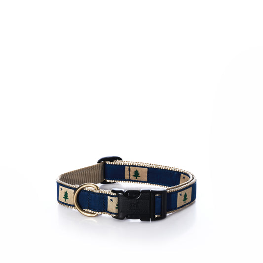 The Belted Cow “Maine Flag Dog Collar 1”“ - Medium is a blue and beige nylon collar made in the USA, featuring a charming pine tree pattern, a sturdy metal D-ring, and a plastic buckle, shown against a white background.