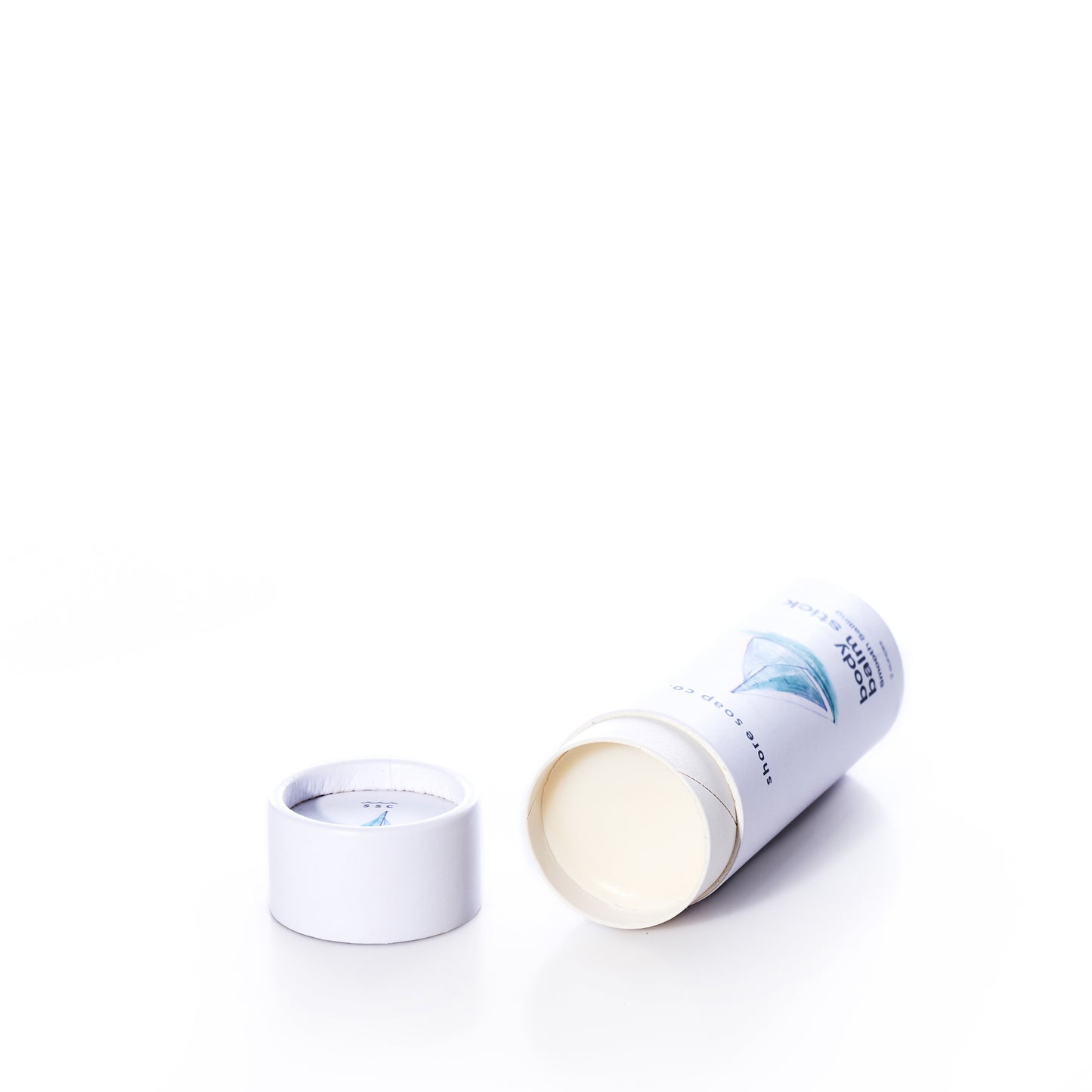 A white cylindrical container of Shore Soap Co’s Smooth Sailing Eco-Friendly Body Balm Stick, shown with its lid off and the solid balm exposed, rests on its side against a white background—ideal for addressing dry skin.