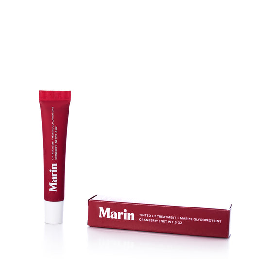 A red tube of Marin Skincare Marin Lip Treatment - Cranberry, infused with hydrating Marine Glycoproteins for superior lip care, stands next to its matching box, both displaying product details in white text against a plain white background. by Sea Bags