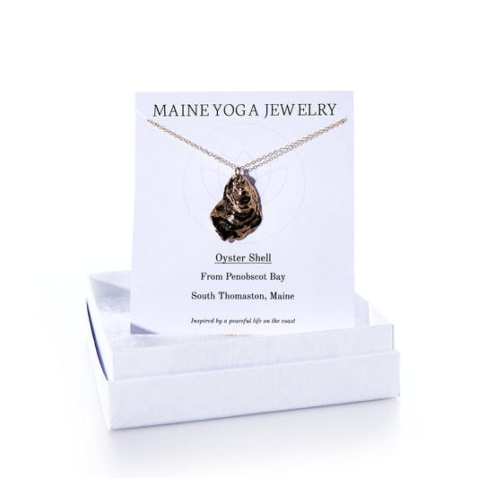 A Pendant Necklace - Large Oyster Bronze from Maine Yoga Jewelry, featured as part of our coastal jewelry collection, is displayed on a branded card and rests atop a white jewelry box. by Sea Bags