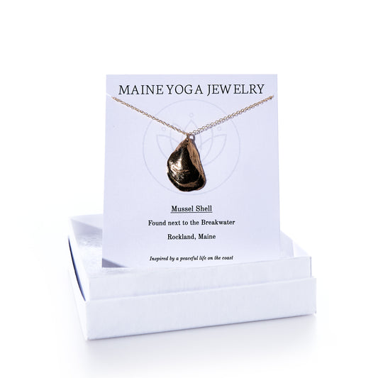 Pendant Necklace - Large Mussel Bronze displayed on a card labeled Maine Yoga Jewelry with descriptive text, set atop a white jewelry box. This elegant piece of coastal jewelry features a beautifully crafted large bronze mussel pendant—perfect for those who treasure seaside memories. by Sea Bags