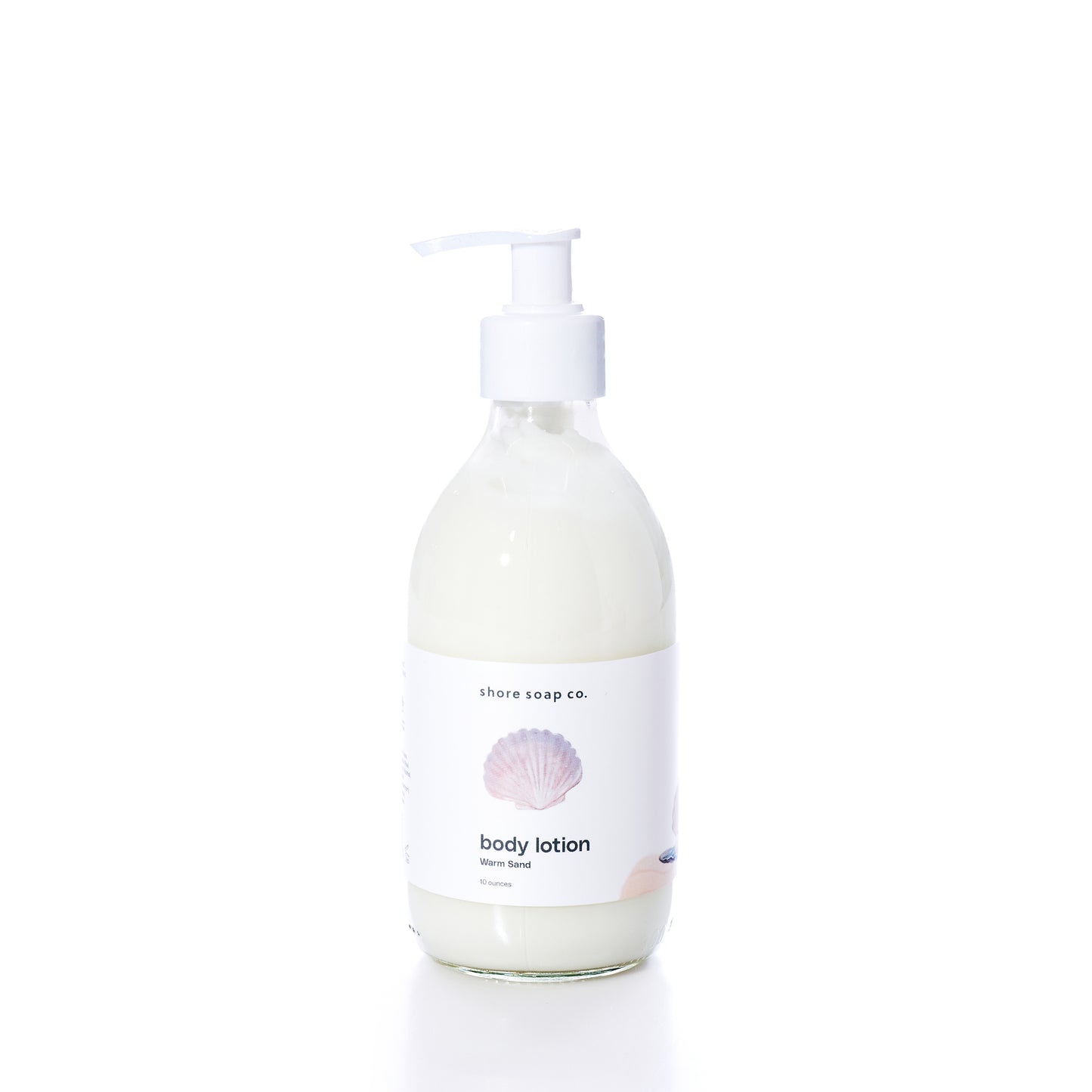 A clear pump bottle of true Warm Sand Eco-Friendly Body Lotion with a white label featuring a seashell graphic, photographed on a white background. Formulated with natural oils to help hydrate dry skin, this lotion provides nourishment while supporting sustainability.