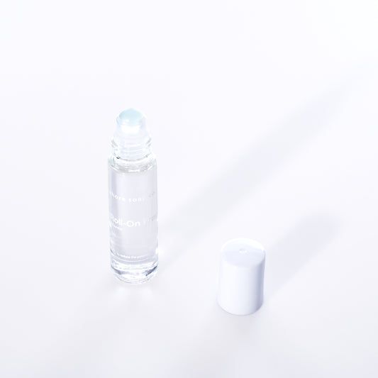 The Atlantic Eco-Friendly Roll-On Fragrance by Shore Soap Co is shown in a clear glass bottle with a white cap placed beside it on a white background, making it perfect for carrying your favorite alcohol-free perfume as a convenient travel fragrance. by Sea Bags
