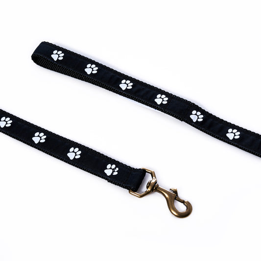 Belted Cow Paw Print Dog Leash in black, featuring a white paw print pattern and a brass metal clip, displayed on a white background.