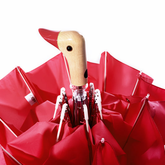 A closed Original Duck Head Umbrella in red, featuring the signature duck head-shaped handle from True, photographed against a white background. by Sea Bags