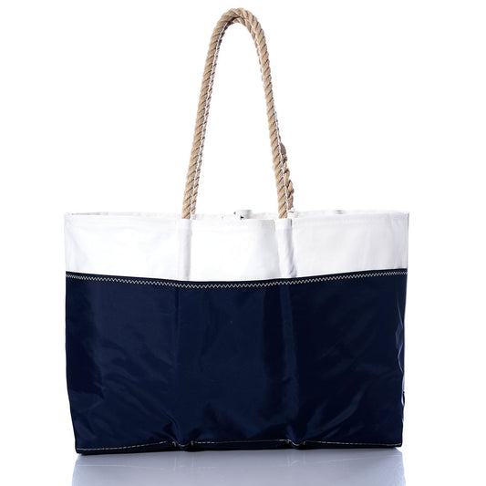 The Sea Bags Vintage Laser Ogunquit Beach Tote features a white upper section, navy blue lower section, and two twisted rope handles. Crafted from recycled sail cloth, this spacious tote is photographed on a white background. by Sea Bags
