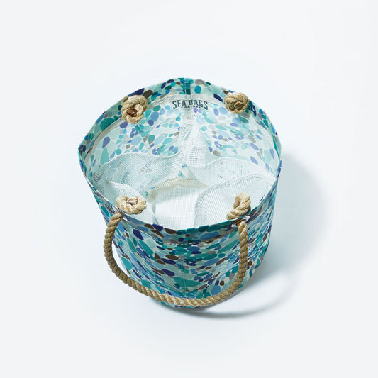 The Sea Bags Sea Glass Print Beachcomber Bucket Bag—a round tote with rope handles and a patterned design—features mesh interior compartments and is photographed from above on a white background. by Sea Bags