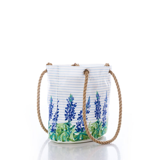 The Lupine on Sailor Stripe Essential Handbag by Sea Bags is a lightweight white bucket bag crafted from recycled sail cloth, featuring blue and green lupine floral designs, thin horizontal blue stripes, and sturdy rope handles. It is displayed against a white background. by Sea Bags