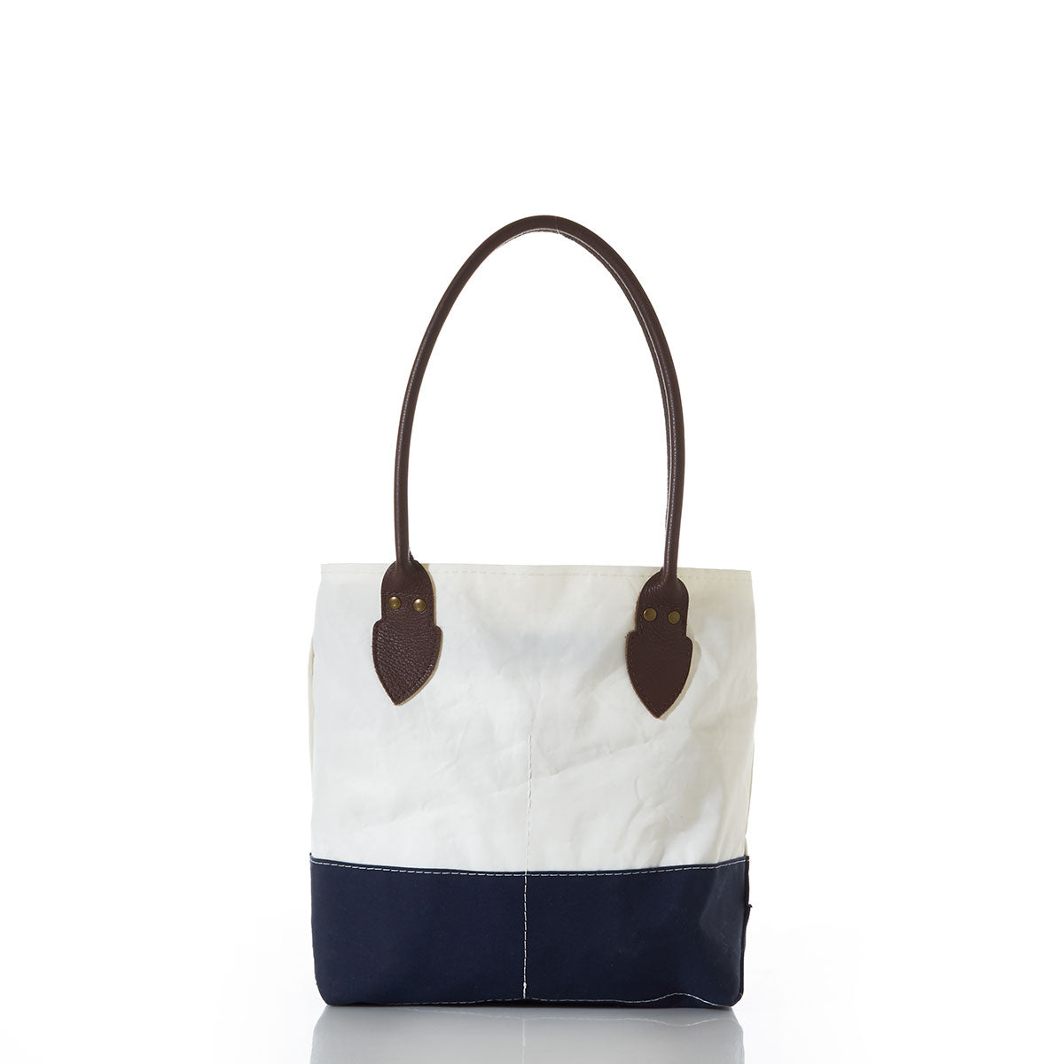 The Sea Bags Chebeague Handbag, from the Chebeague Collection, is a nautical tote featuring a white upper section, navy blue bottom, and dark brown handles. Crafted from recycled sail cloth for both style and sustainability, this two-tone bag is photographed on a white background. by Sea Bags