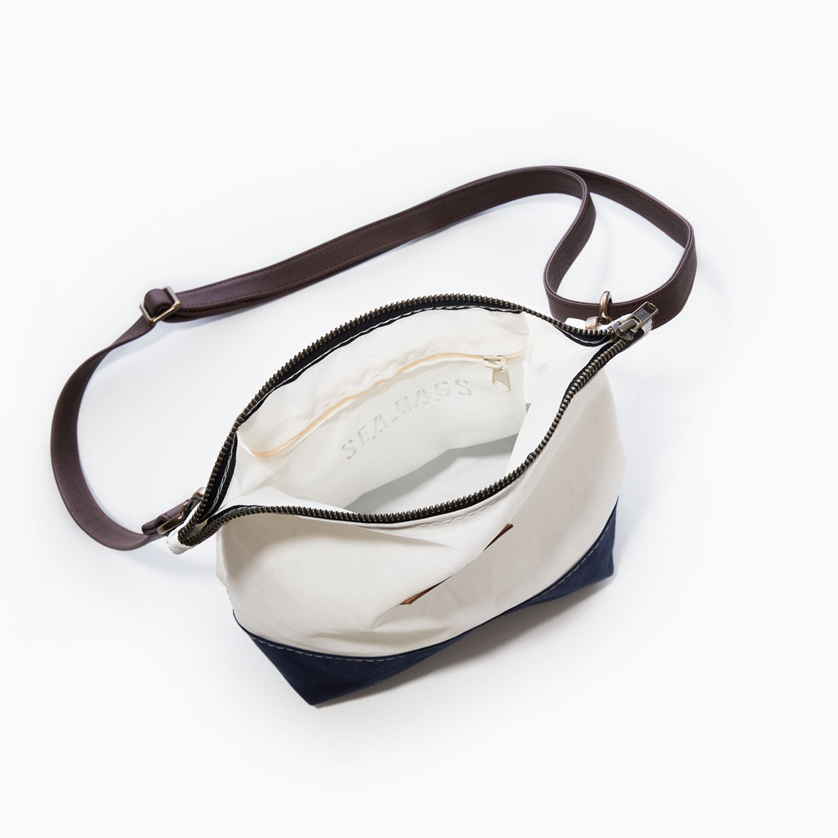 The Chebeague Crossbody Bag by Sea Bags, crafted from durable Dacron sailcloth, features a dark adjustable strap, white interior lining, zippered pocket, and an open main compartment. Photographed from above on a white background. by Sea Bags