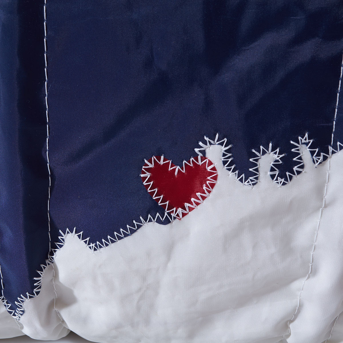 Close-up of the Custom Maine Tote by Sea Bags, featuring navy blue and white sections with zigzag stitching and a red heart applique near the center—a charming detail that makes this bag a perfect personalized tote or an ideal gift from Maine. by Sea Bags