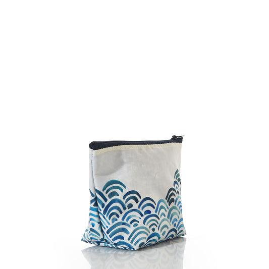 The Watercolor Waves Cosmetic Bag by Sea Bags features a blue wave pattern and is crafted from recycled sailcloth; this eco-friendly accessory stands upright on a white reflective surface, offering both style and functionality for travel. by Sea Bags