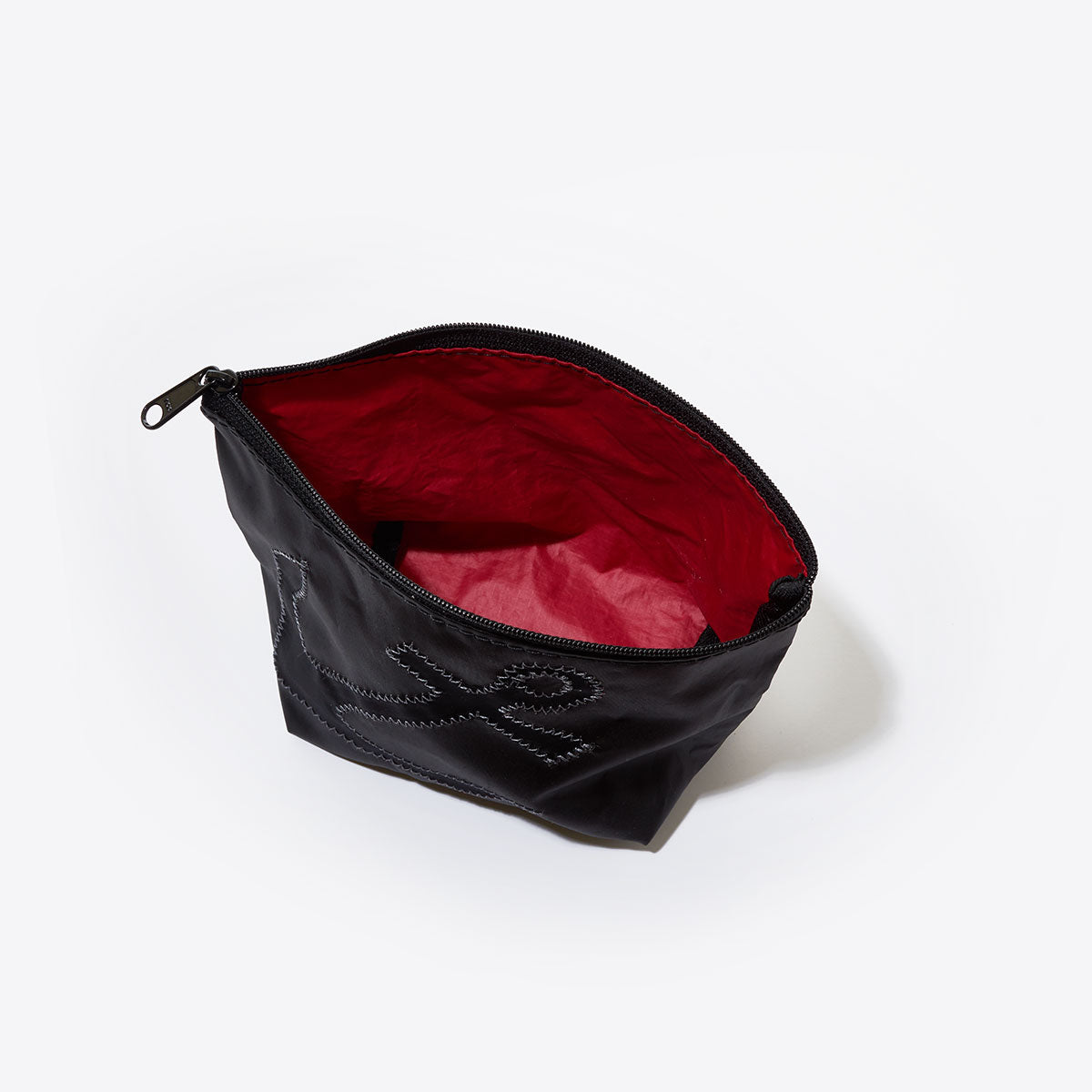 The Sea Bags Black-on-Black Anchor Cosmetic Bag, made from recycled sailcloth and featuring a bold anchor design with a vivid red interior, is displayed open against a plain white background. by Sea Bags