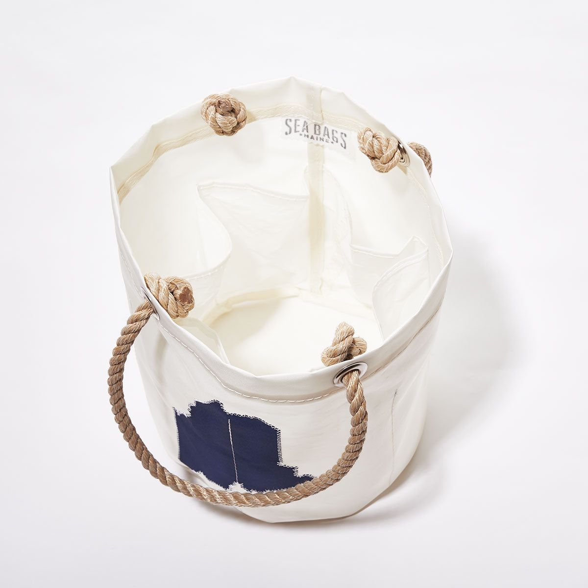 State of Maine Beverage Bucket by Sea Bags, crafted from recycled sail cloth in white, features rope handles, navy Maine graphic detail, interior pockets, and a Sea Bags label inside. The bucket bag stands upright on a white background. by Sea Bags
