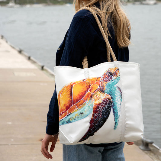 A woman stands on a dock by the water, carrying the Sea Bags Multicolor Sea Turtle Medium Tote with thick rope handles over her shoulder. by Sea Bags