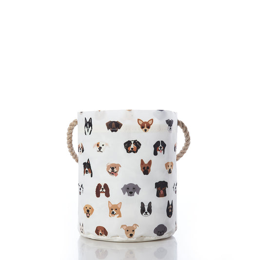 The Sea Bags Popular Pups Print Bucket Bag is a white fabric dog storage basket featuring sturdy rope handles and decorated with colorful cartoon dog faces of various breeds on a plain white background. This delightful pet organizer helps keep your furry friends toys tidy while adding a playful touch to any room. by Sea Bags
