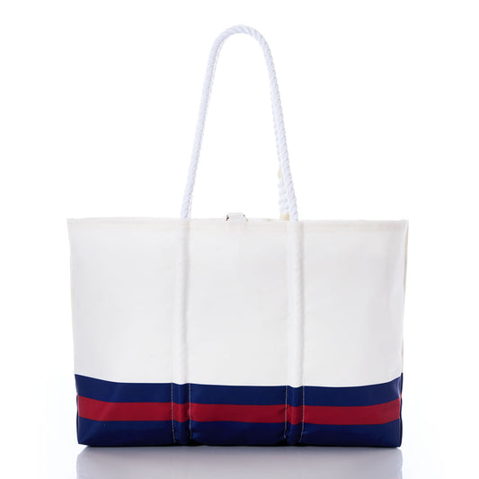 Introducing the New York Giants Tailgate Tote by Sea Bags: a white tote bag featuring blue and red horizontal stripes at the bottom and two sturdy white rope handles, displayed on a white background. Crafted from recycled sail cloth, this eco-friendly tote blends nautical style with sustainable design for a fashionable and earth-conscious way to support your team. by Sea Bags