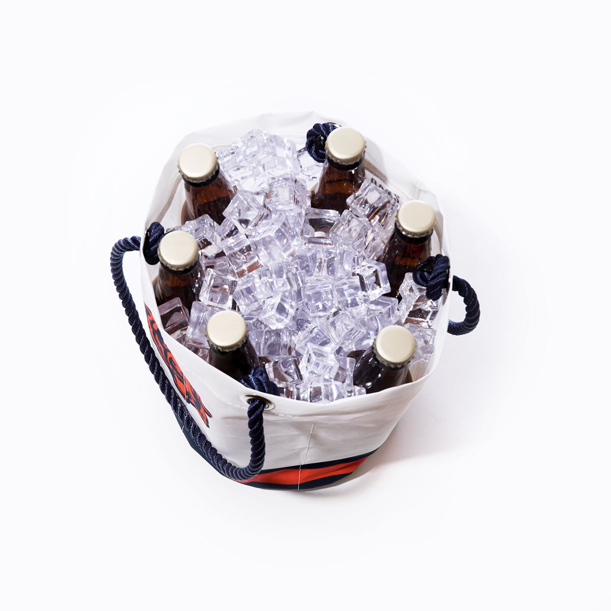 Six brown glass bottles with gold caps are placed in the Sea Bags Chicago Bears Beverage Bucket, made from white recycled sail cloth and filled with ice cubes. The cooler features dark blue rope handles and red and blue stripes along the side. by Sea Bags