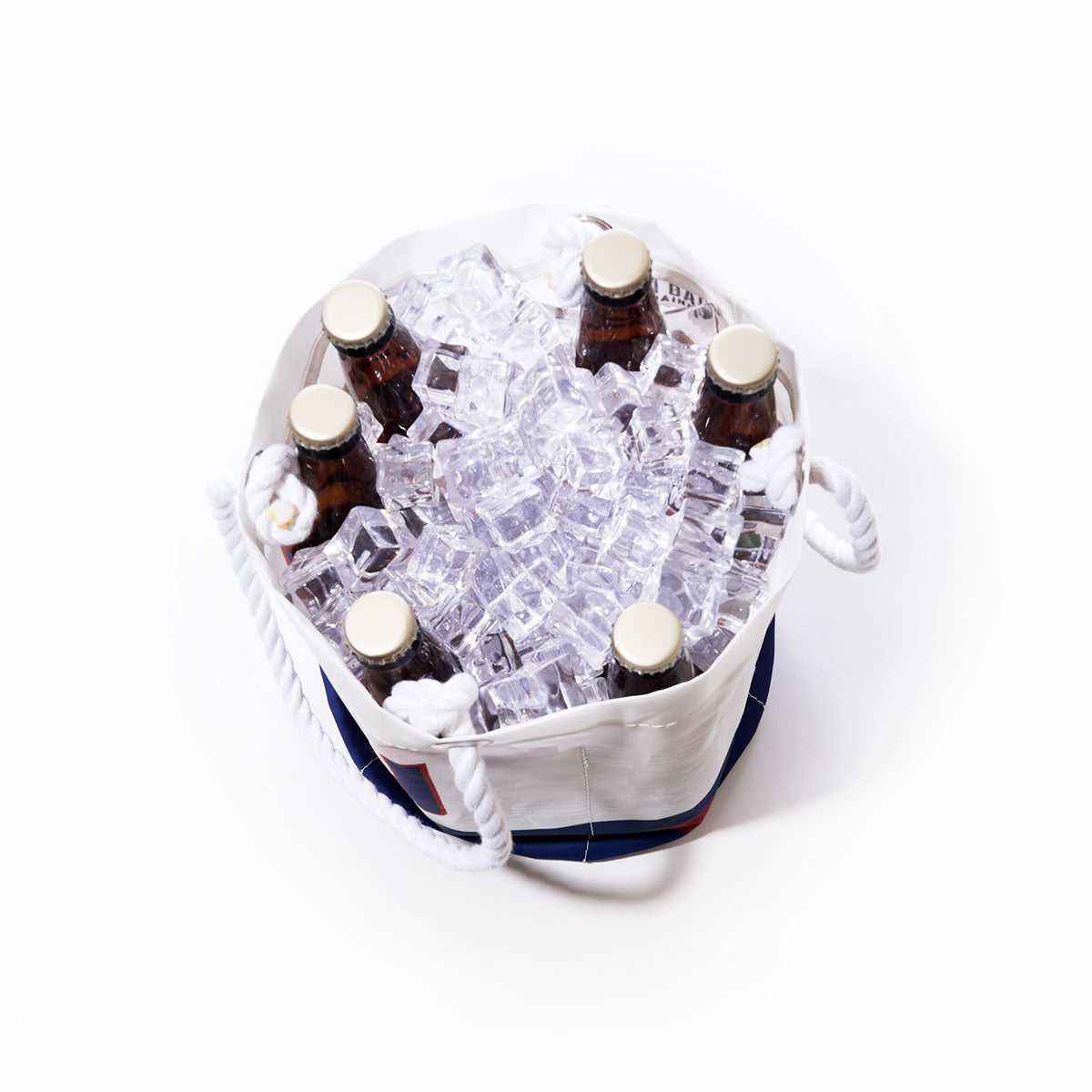 Six brown glass bottles with gold caps are arranged upright in a Sea Bags New York Giants Beverage Bucket, crafted from white sail cloth and filled with ice cubes, viewed from above against a plain white background. by Sea Bags