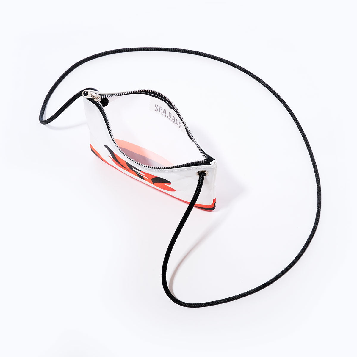 The Sea Bags Cincinnati Bengals Slim Crossbody is a small rectangular bag with a long black strap and a white body made from recycled sail cloth, featuring a top zipper and an abstract red and black design on the front, shown photographed from above on a white background. by Sea Bags