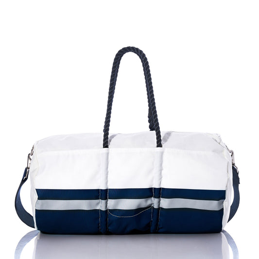 The Sea Bags Dallas Cowboys Duffel, crafted from recycled sail cloth, features a white design with navy blue accents, sturdy navy rope handles, and a detachable shoulder strap—evoking the look of an NFL duffel. Displayed on a reflective surface, this bag combines durability and style for your travels. by Sea Bags