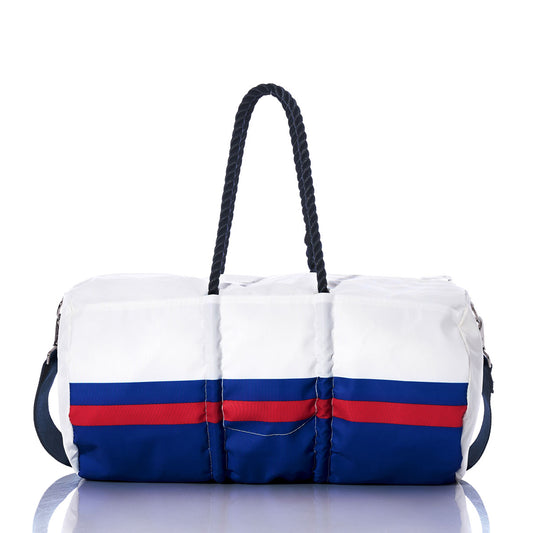 The Sea Bags Buffalo Bills Duffel features eco-friendly construction from recycled sail cloth in white, accented with blue and red horizontal stripes, navy rope handles, and a detachable shoulder strap. Displayed on a reflective surface, this unique duffel bag is the perfect sporty game day accessory for Buffalo Bills fans. by Sea Bags