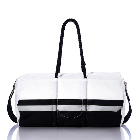 A Las Vegas Raiders Duffel by Sea Bags, made from recycled sail cloth, features a two-tone design with a white upper, black base, black side strap, and two black twisted handles, displayed on a reflective surface. by Sea Bags