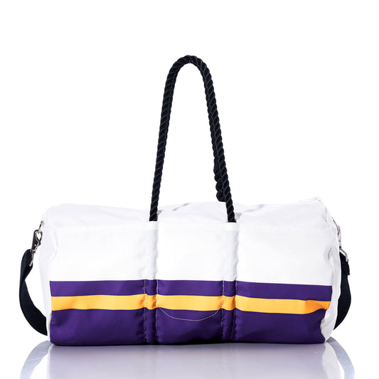 The Sea Bags Minnesota Vikings Duffel, crafted from recycled sail cloth, features purple and yellow stripes inspired by a classic Vikings bag. It is designed with black rope handles and a black adjustable shoulder strap, and is shown on a reflective surface. by Sea Bags