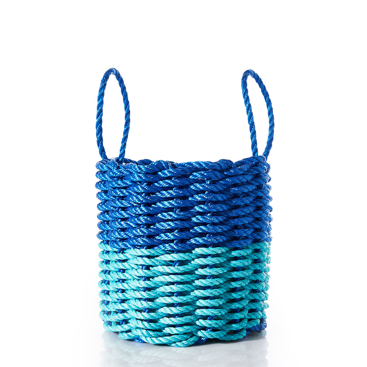 The Fisherman Rope Basket - Blue Teal by Custom Cordage / DBA Maine Rope Mats is a round, handcrafted basket with two handles, made in Maine from eco-friendly materials. It features thick blue and teal braided rope arranged in a horizontal pattern and is shown on a white background. by Sea Bags