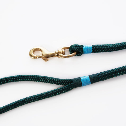 The Maine Rope Dog Leash - Hunter Green by Custom Cordage / DBA Maine Rope Mats features a dark green braided yacht rope with blue accent bands and a brass clip, displayed on a white background. This handmade leash blends nautical style with durable craftsmanship. by Sea Bags