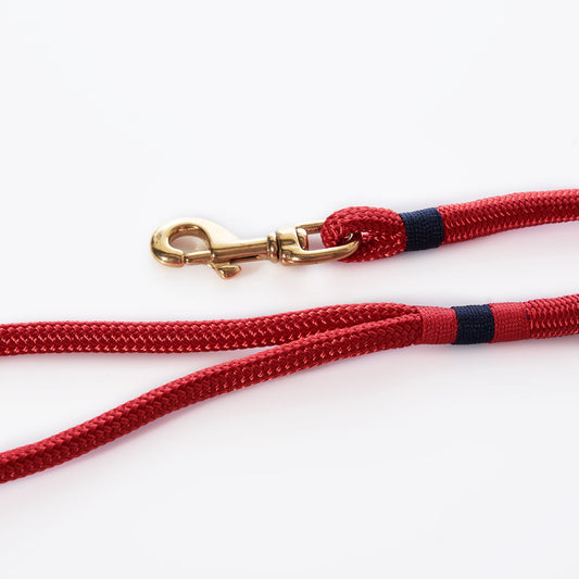 The Maine Rope Dog Leash - Deep Red by Custom Cordage / DBA Maine Rope Mats is a handmade leash crafted from red braided rope with black accents and finished with a brass swivel snap hook. Coiled on a white background, this classic nautical-style leash is perfect for adventurous pets who love the yacht braid look. by Sea Bags
