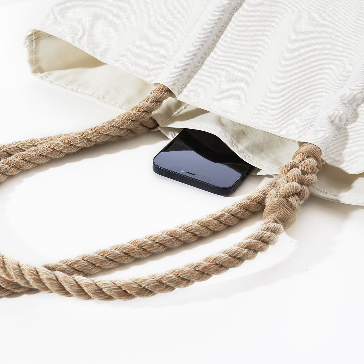 A black smartphone rests inside an open Sea Bags Acadia National Park Tote, crafted from white recycled sail cloth with thick rope handles, set against a white background and echoing the timeless style of coastal Maine. by Sea Bags