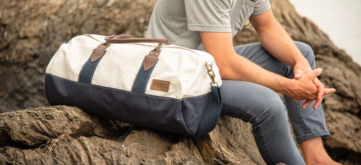 Person on the rocky coastline sitting with a weekender duffel bag made of upcycled sails