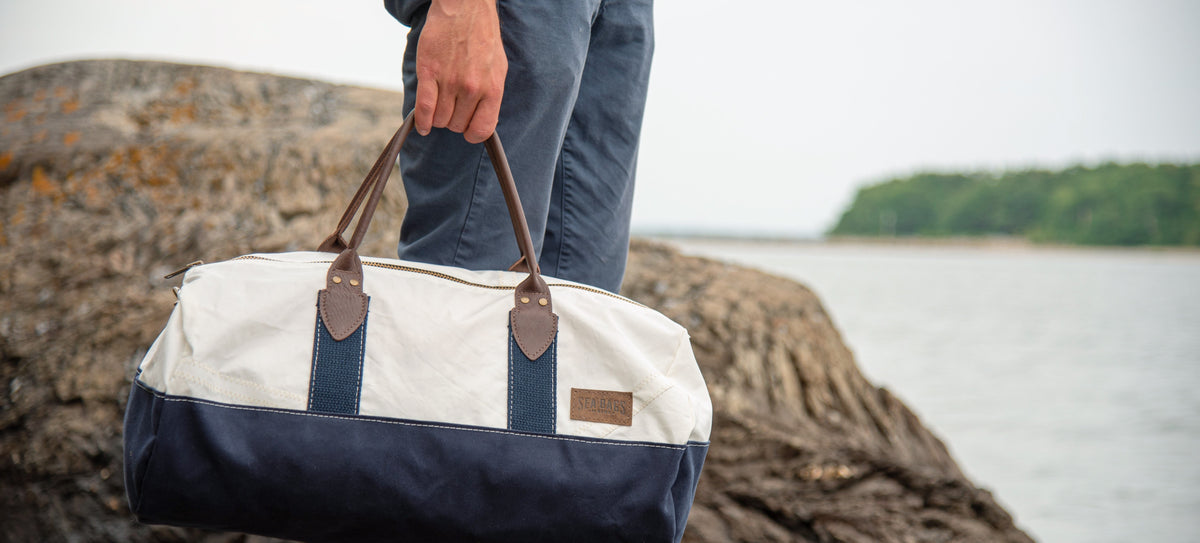 Man carrying a handsome travel duffel on the rocky coast