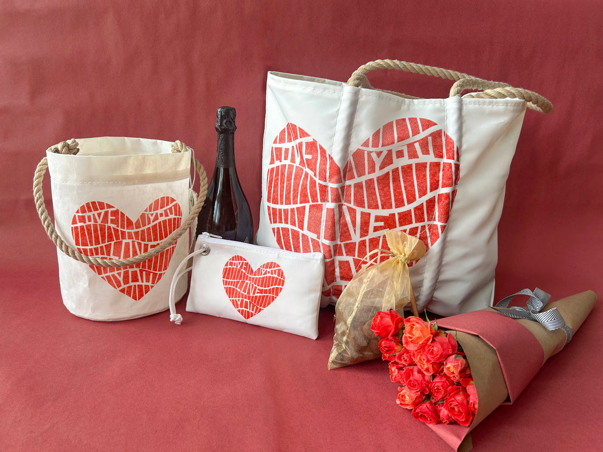 Tote bag, pouch, and basket with red heart designs, a bottle, a bouquet of red and orange roses, and a bag of dried flowers on a red background.