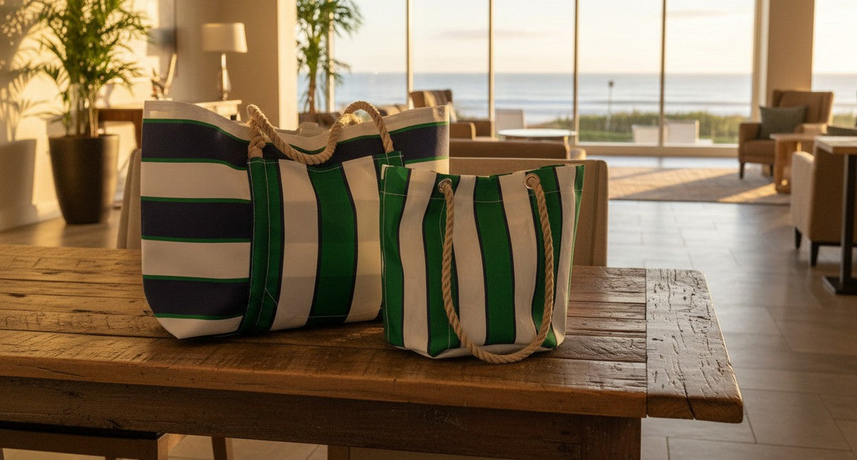 Two striped tote bags with rope handles sit on a wooden table in a sunlit room with large windows, indoor plants, and a view of the ocean in the background.