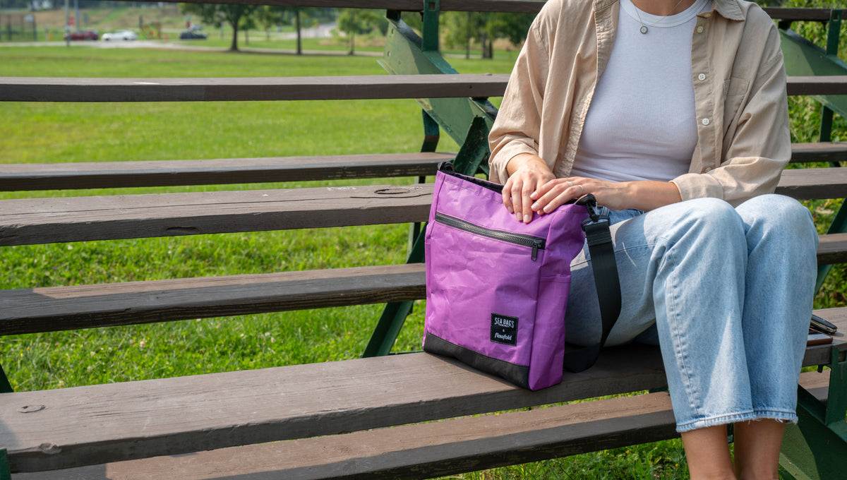 Purple Voyager crossbody bag on a park bench