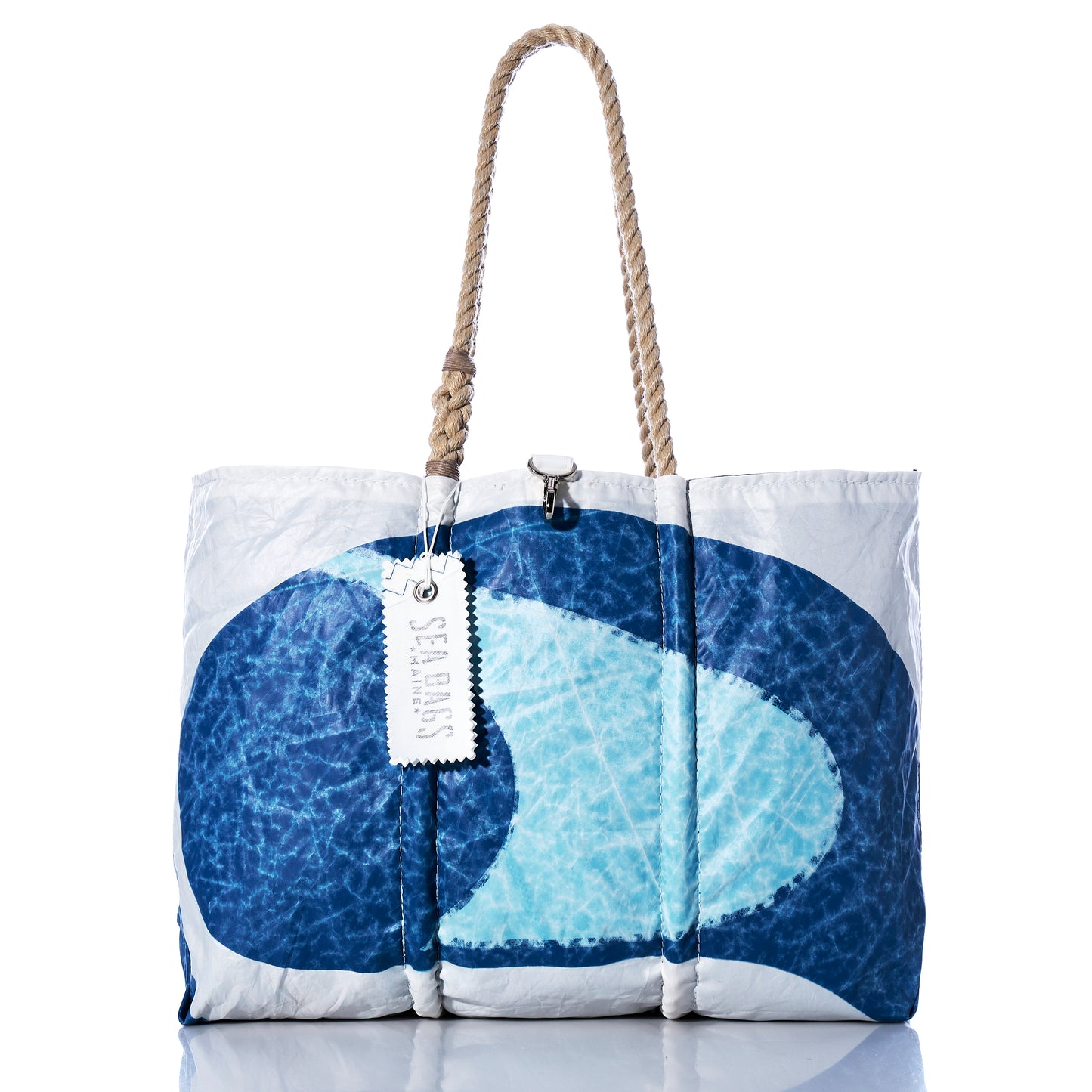 The Auction Sun-Washed Sailboat Large Tote by Sea Bags is a large white and blue patterned sail tote featuring thick rope handles, a clasp closure, and a rectangular hanging tag labeled “Sea Bags,” photographed against a white background. This striking nautical tote embodies classic coastal style, making it the ideal companion for seaside adventures.