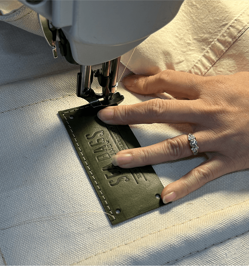 Sewing a leather Sea Bags patch onto a canvas heritage tote bag in Maine